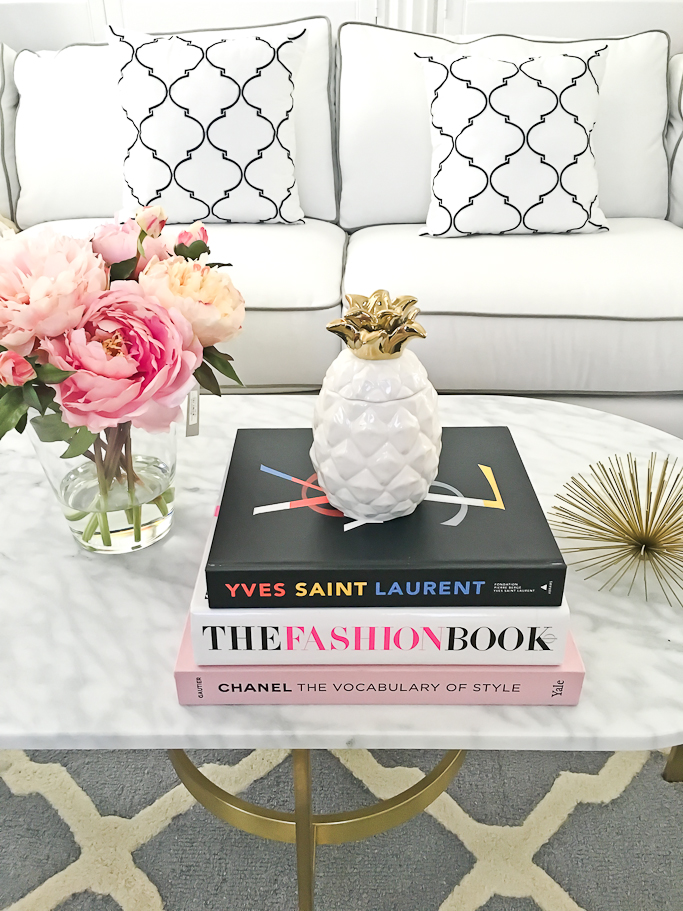 Chanel The vocabulary of style book, faux silk peonies in glass vase, Gold urchin, Home Decor, Oval marble coffee table, Pineapple candle, The Fashion Book, TRELLIS ACCENT PILLOWS, White sofa with grey piping, Yves Saint Laurent YSL book