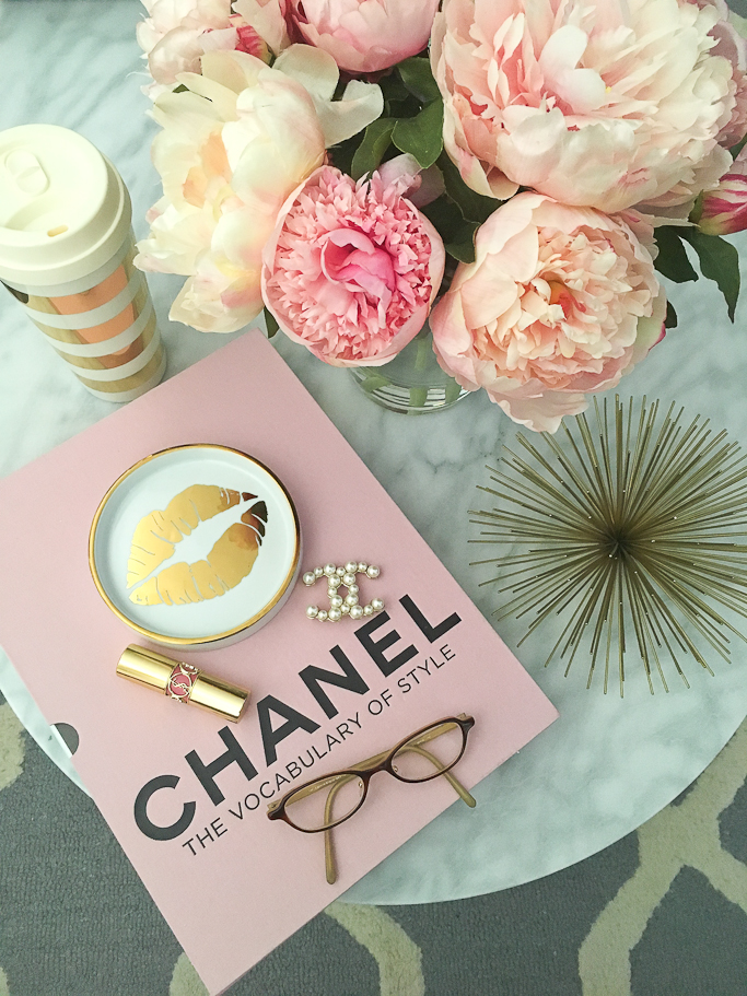 Chanel pearl brooch, Chanel The vocabulary of style book, faux silk peonies in glass vase, Gold urchin, Grey trellis tufted rug, Kate Spade gold striped thermal mug, Oval marble coffee table, Rosanna Gold Trim Porcelain Wine Coaster, YSL lipstick
